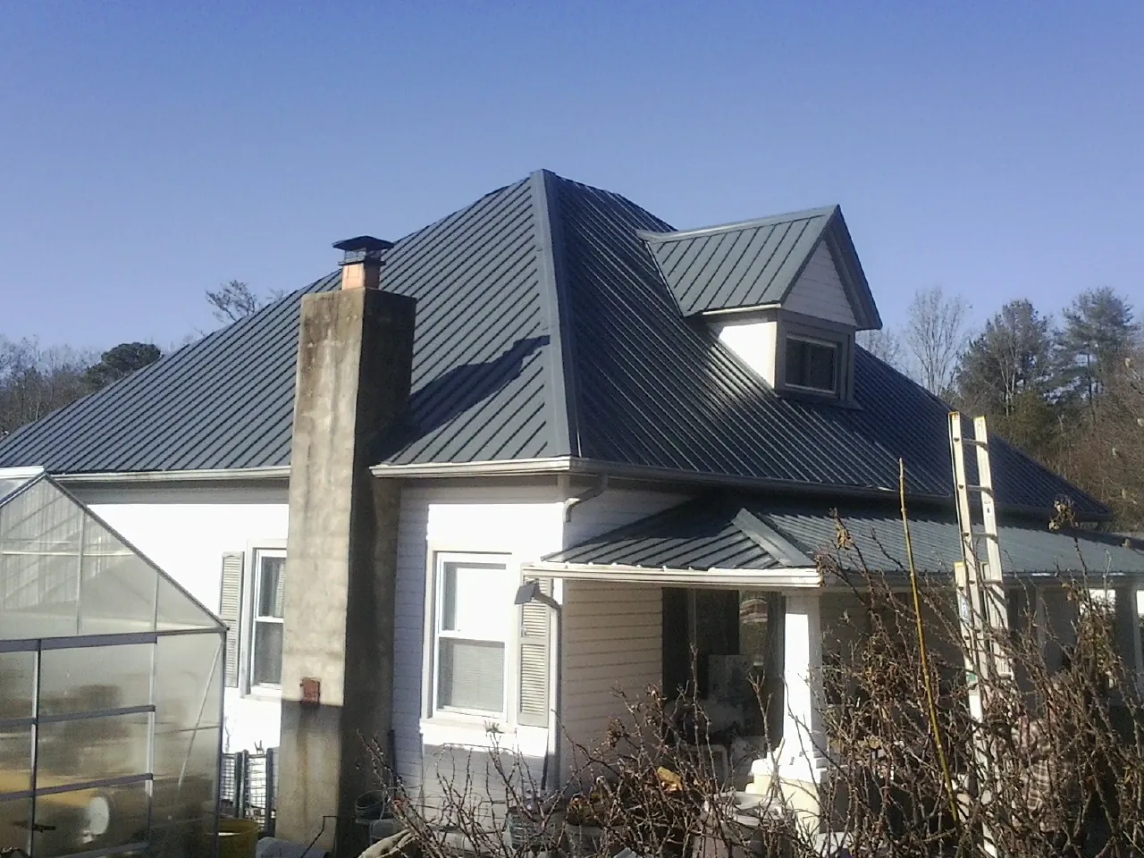 Dark blue standing seam metal roof on a white farmhouse with dormer — Slate & Tile Roof Repair by Roofing Brothers in Little Silver