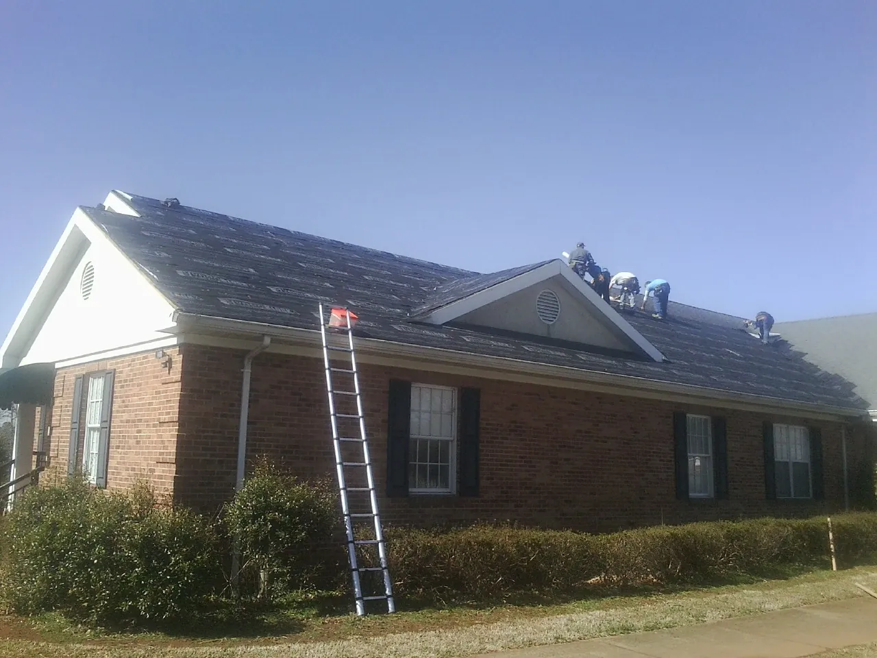 Crew tearing shingles off a brick ranch roof with a ladder set — Metal Roof Repair work by our crew in Little Silver