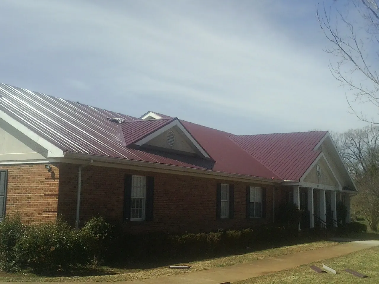 Red metal roof with gabled entries on a long brick building, from a Hail Damage Roof Repair job in Little Silver
