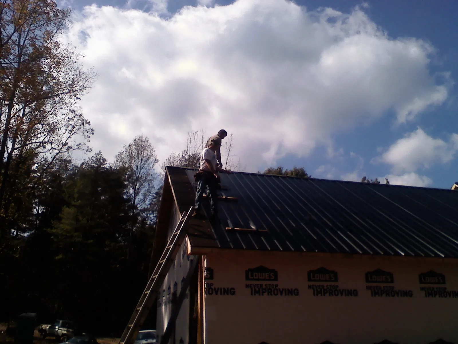 Roofer fastening dark metal panels high against a cloudy sky, from a Roof Inspection job in Little Silver