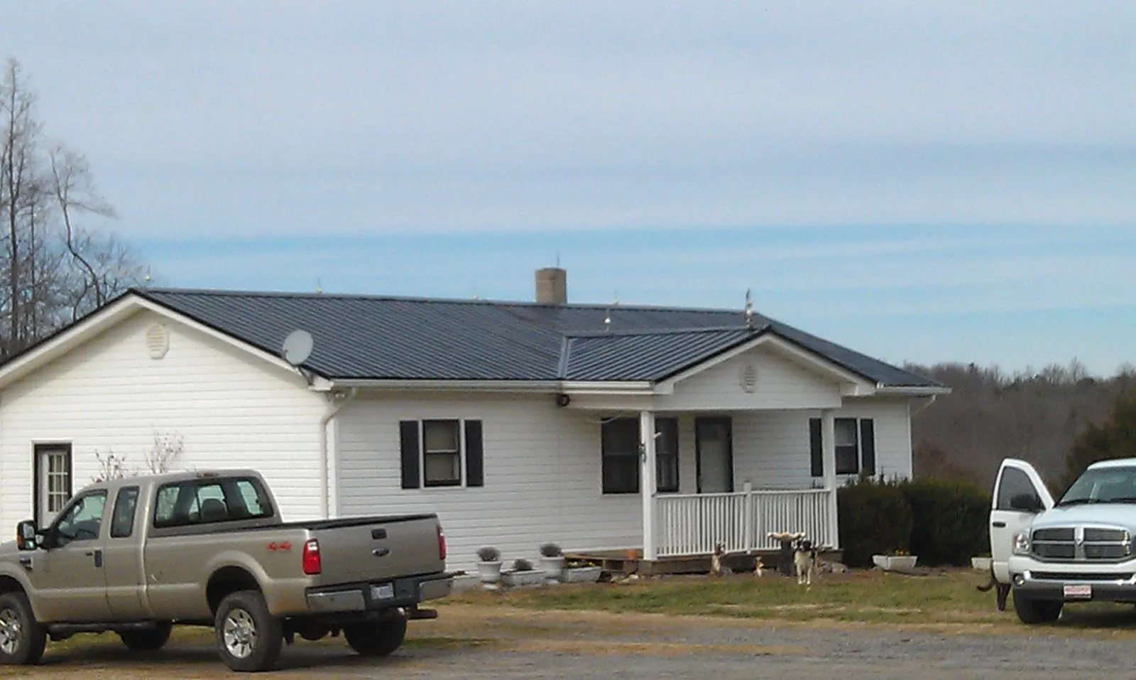 Finished dark metal roof on a white ranch home with work trucks parked in Little Silver