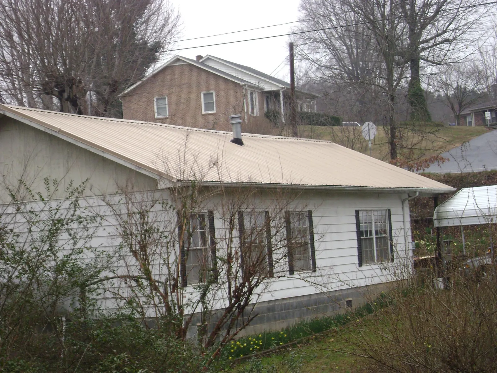Tan metal roof on a white sided house set into a hillside — Commercial Roofing by Roofing Brothers in Little Silver